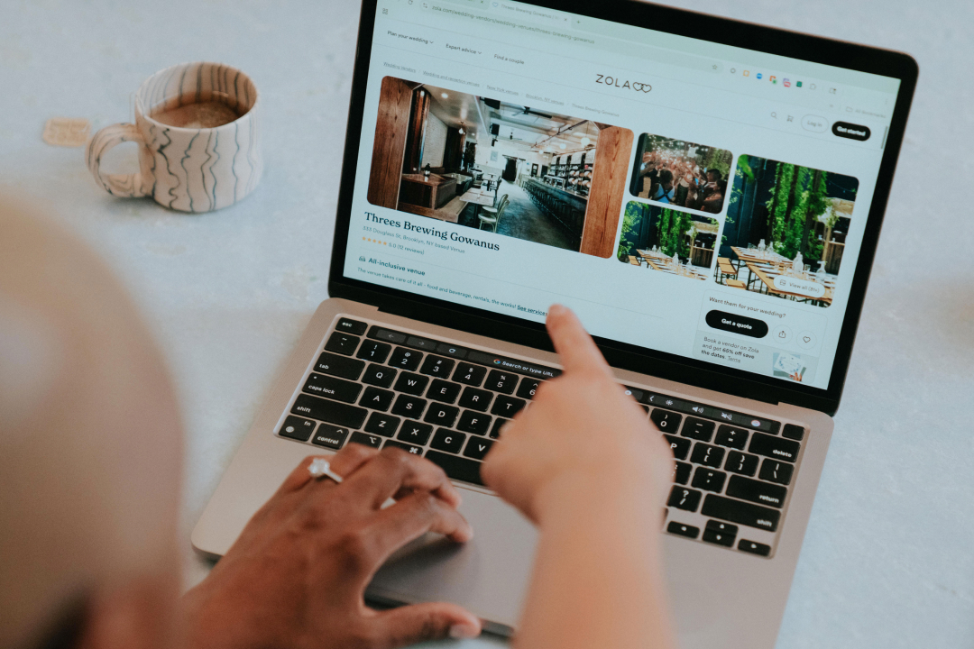 Person browsing Zola wedding website showing Threes Brewing Gowanus venue, with patterned coffee mug nearby.