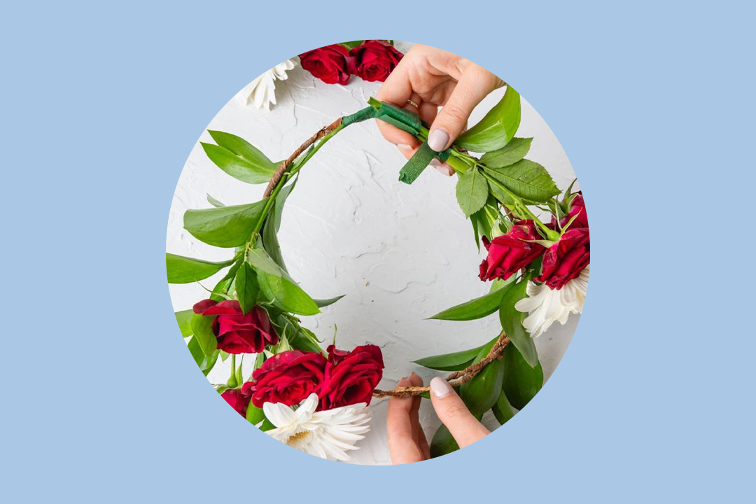 woman making a flower crown of white and yellow daisies and red roses