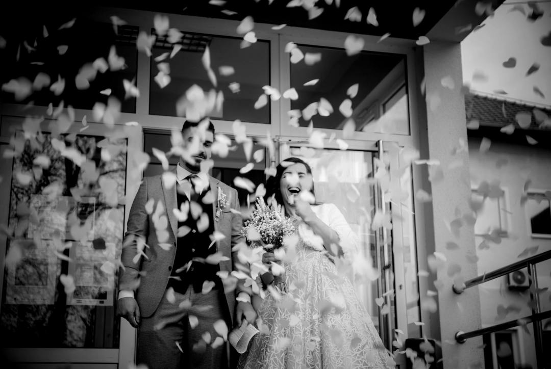 Newlywed couple standing in front of a glass door as confetti is being tossed at them