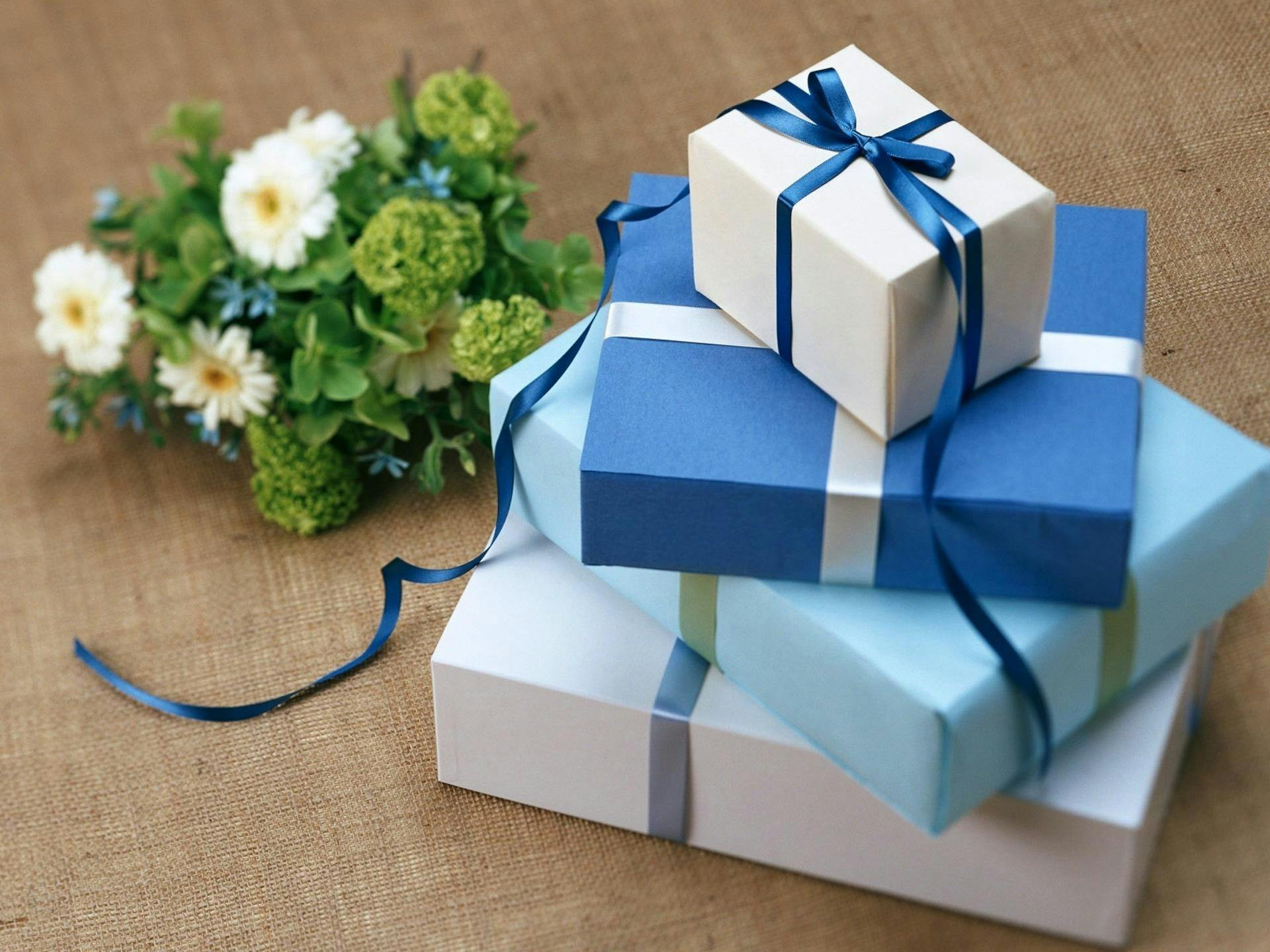 Stack of blue wedding gift boxes on a table next to a white flower arrangement