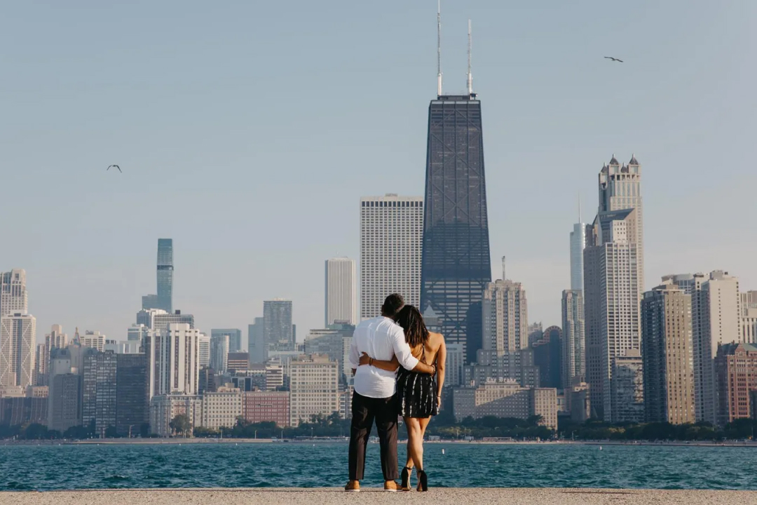 Couple embracing while admiring Chicago skyline with John Hancock Center from lakefront on a clear day.
