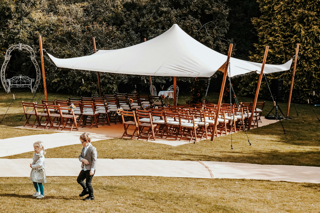 An outdoor wedding venue overlooking the ocean is set up with white chairs and a floral altar. Text on the image says "Average Wedding Venue Cost: Budget Guide and Pricing" with icons for "Location," "Seasonality," and "Services included."