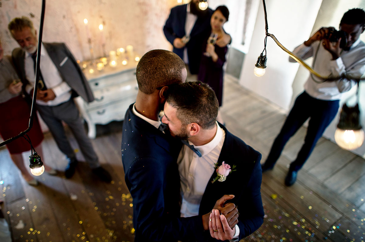 A groom and groom are shown slow dancing on the dance floor as guests watch and take photos, indicating they hired a wedding DJ and vetted them with appropriate questions to ask a wedding DJs. 