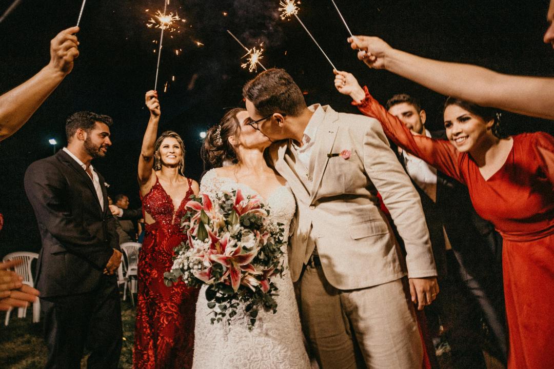 Bride and groom kissing while wedding party holds sparklers celebrating