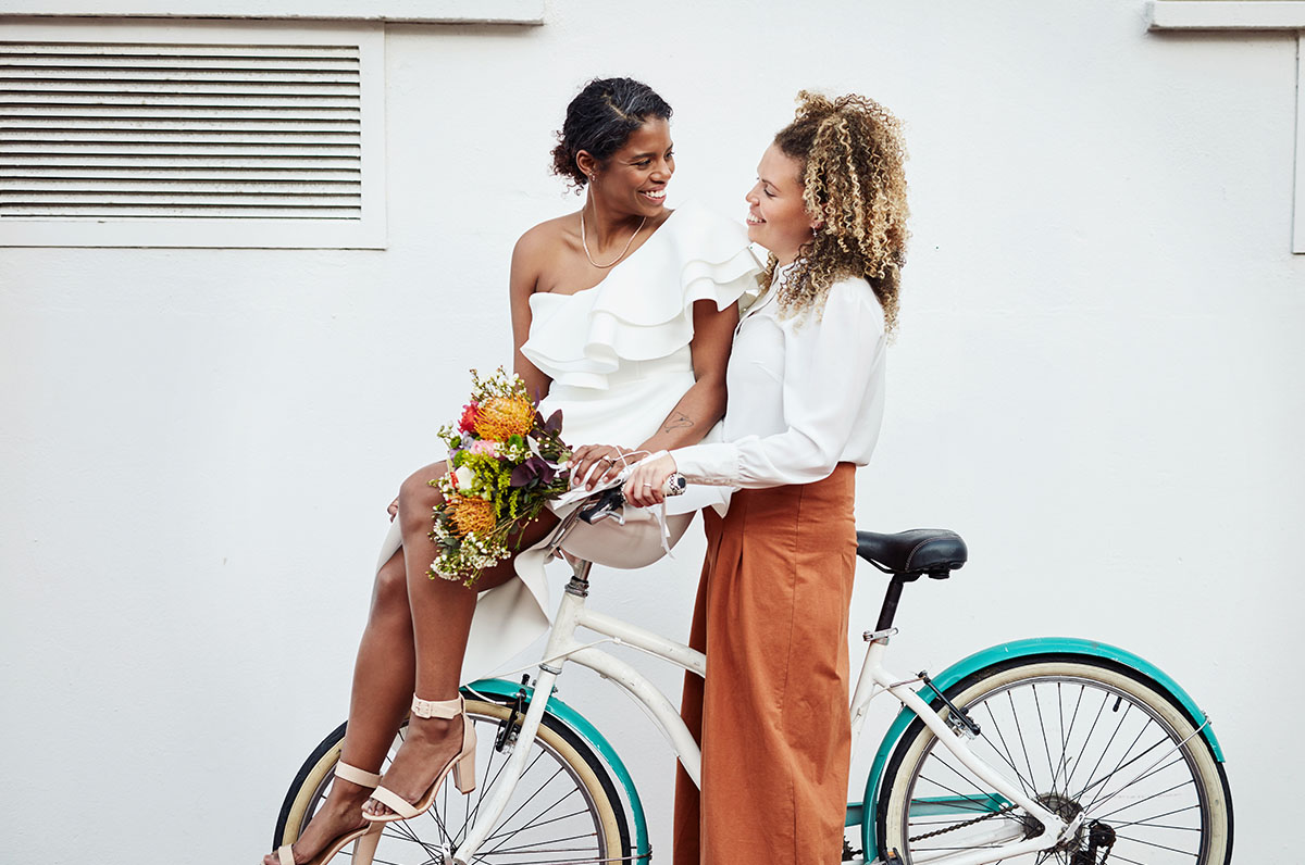 Two newlyweds post with a bicycle, one of the many new wedding traditions to try in 2023.