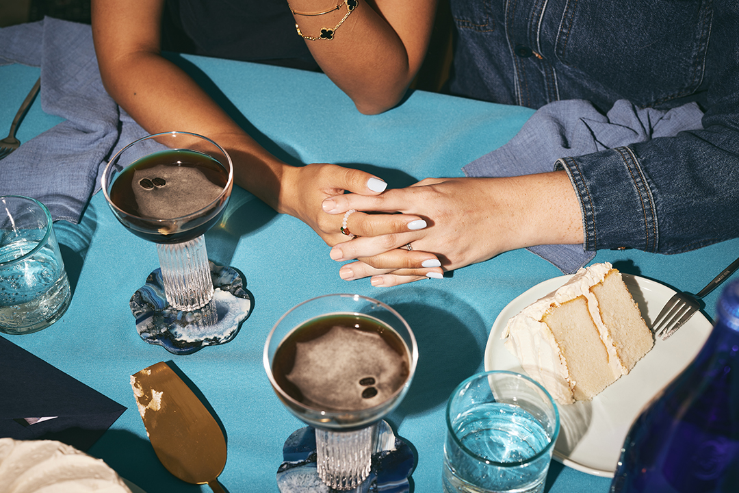 Pair of hands holding on a blue table with espresso martinis and a slice of cake.