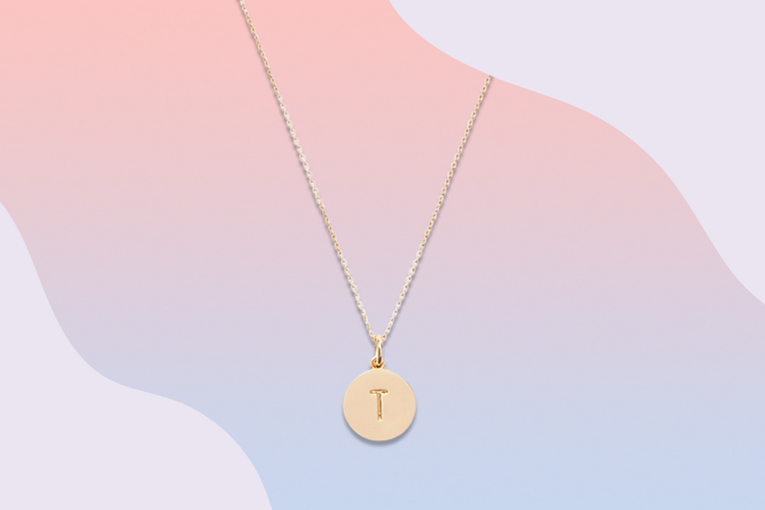 Gold necklace with letter "T" on graphic background
