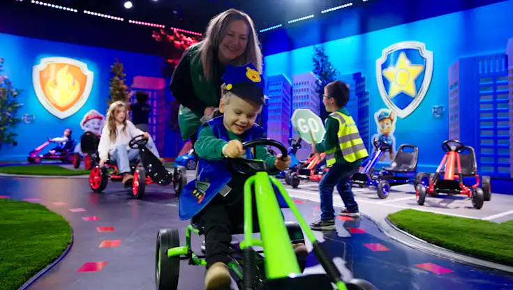 Looking for things to do as a family in Atlanta? Explore The Paw Patrol Experience Only at CAMP in Atlanta. Image is a kid driving a ride on toy in a Paw Patrol costume on a race track. 
