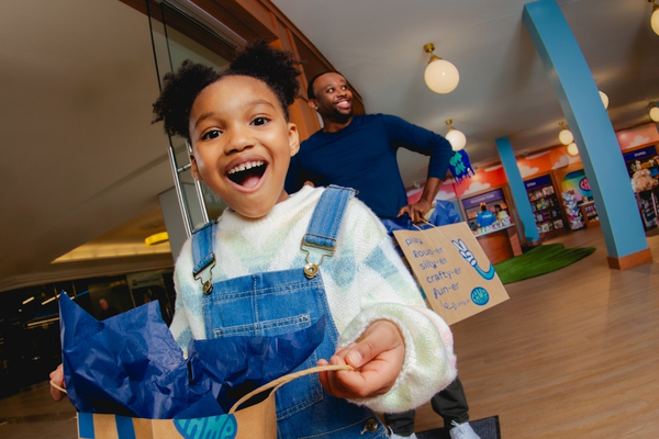 Child smiling while holding a bag of merchandise after shopping the CAMP store.