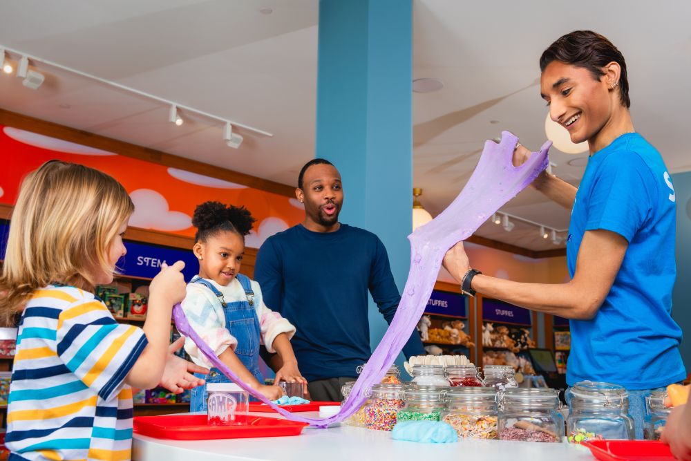 CAMP counselor at the Slime Bar helping child make purple custom slime. Your CAMP Counselor walks kids through the whole process.