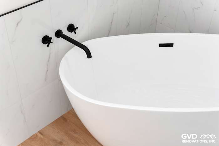 Modern bathroom featuring a freestanding white tub with sleek black faucet against white marble tile wall in Paradise, CA
