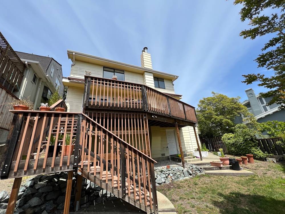 Two-story home with wood deck and staircase, surrounded by greenery in Sacramento area