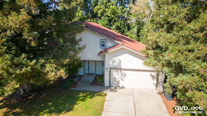 Updated Sacramento home featuring James Hardie lap siding, trim, and a red roof in a lush tree-lined setting