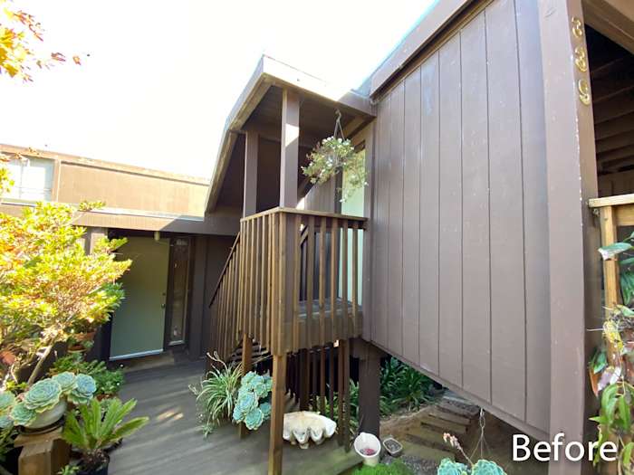 Before remodeling, this home features dark brown siding and wooden stairs with surrounding landscaping