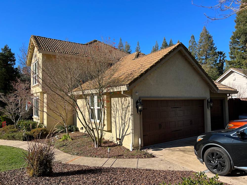 A beige stucco home with a tiled roof, featuring a two-car garage in Sacramento's sunny landscape