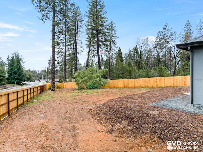 Newly cleared yard area with wood fencing, surrounded by tall pine trees in Paradise, CA
