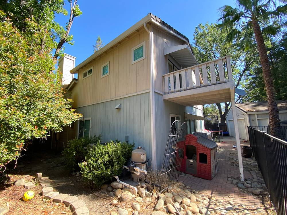 Residential backyard in Sacramento, featuring a concrete patio, greenery, and wooden balcony
