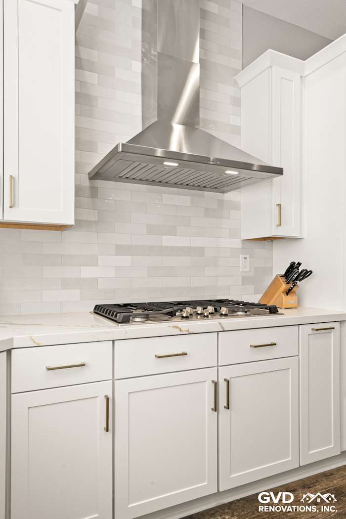 White kitchen cabinets with gold hardware, modern range hood, and gray subway tile backsplash in Roseville, CA remodel