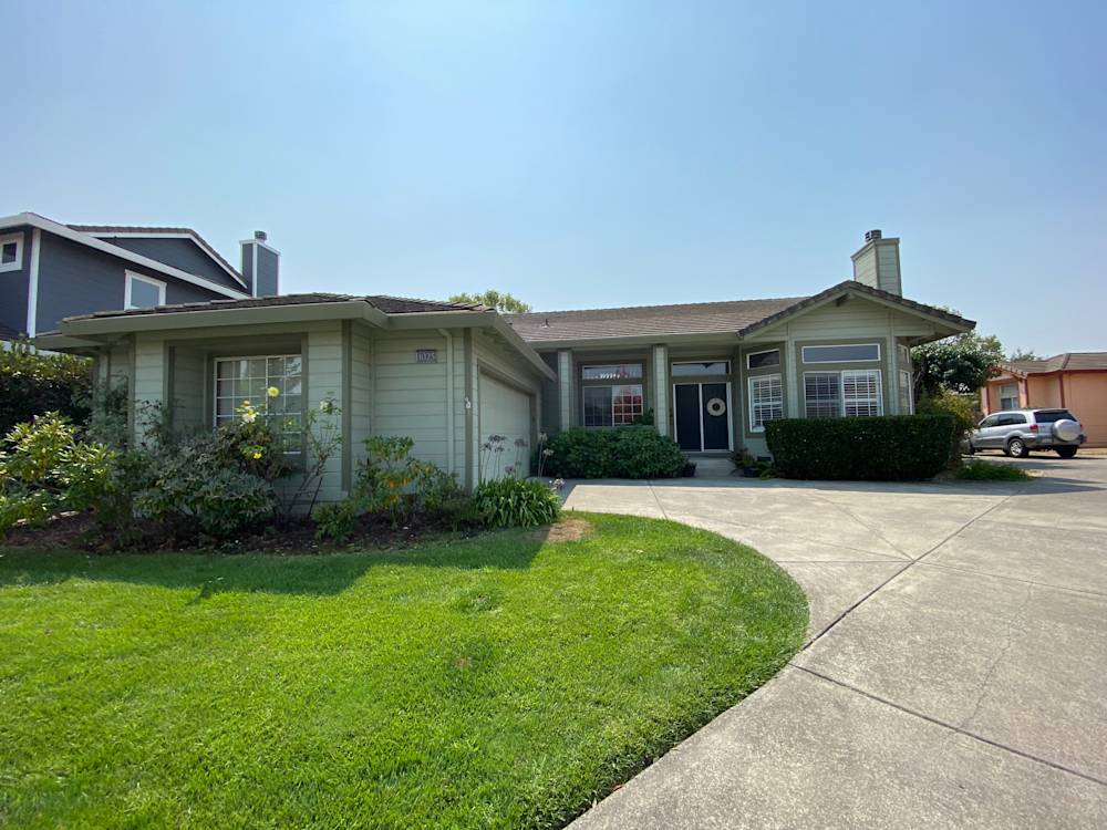 Single-story home in Sacramento with muted green siding and landscaped front yard, features concrete driveway