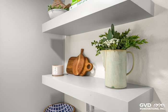 Modern kitchen shelf with white floating shelves, ceramic vase, wooden cutting board, and decorative plants