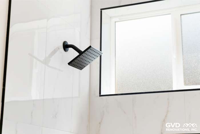 Modern black rainfall showerhead installed on marble-tiled bathroom wall with frosted window in Paradise, CA
