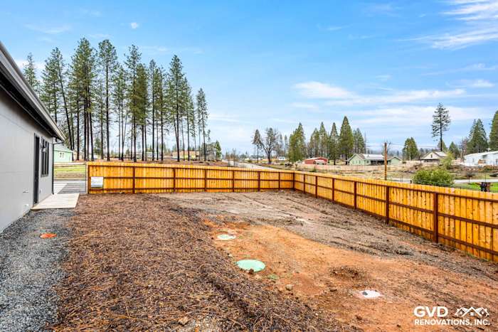 Newly constructed home exterior with fenced yard, gravel landscaping, and surrounding trees in Paradise, CA