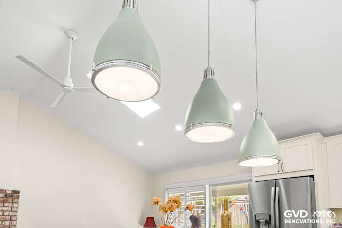 Three mint green pendant lights hang above a modern kitchen island in a bright, remodeled space