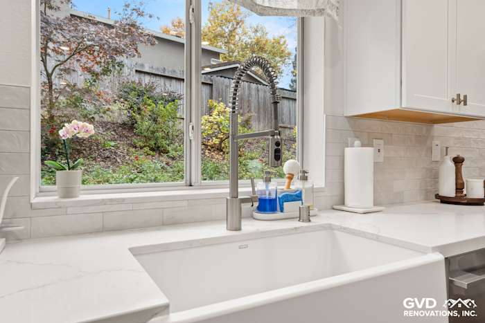 Sleek kitchen sink with modern faucet, white Custom Vadara Bronzo countertop, and view of green backyard