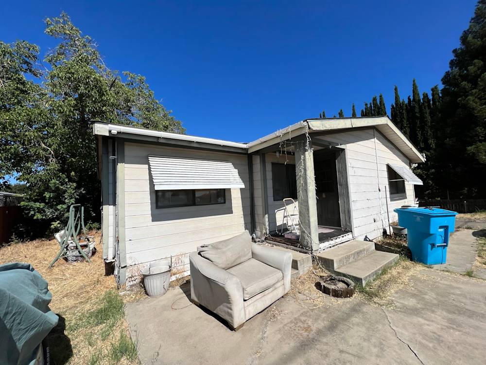 Weathered single-story home with peeling paint, overgrown yard, and an old sofa in Sacramento