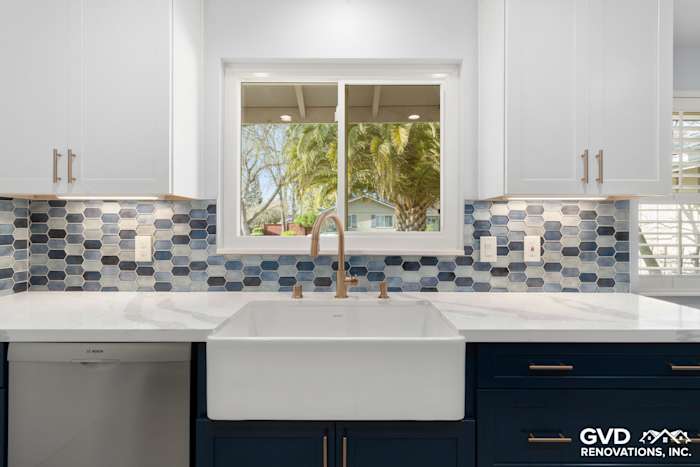 New kitchen remodel featuring blue hexagon backsplash, white cabinetry, farmhouse sink, and gold fixtures