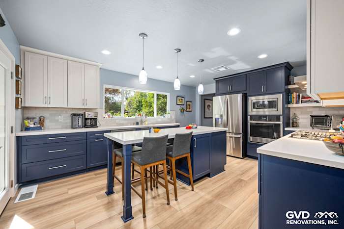 Modern kitchen with navy blue cabinetry, white countertops, and pendant lighting, featuring an open layout and dining area