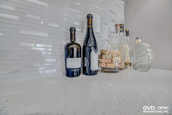 Sleek kitchen countertop with white quartz, modern backsplash, wine bottles, and decorative glass elements