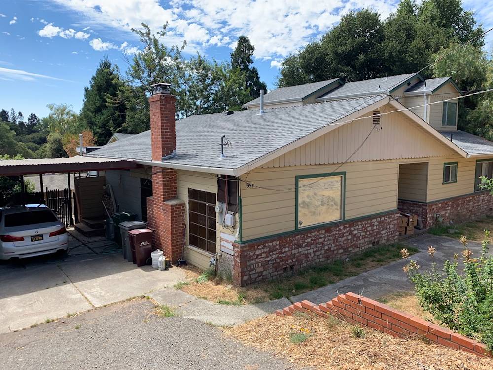 Worn exterior of home with outdated siding and brick, cluttered driveway