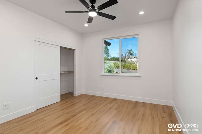 Bright interior bedroom with light wood flooring, white walls, and large window showcasing outdoor views
