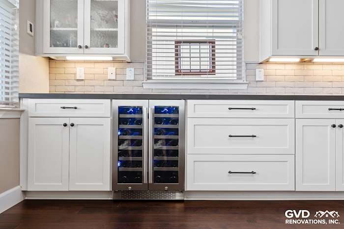 Modern kitchen cabinetry with white shaker doors, gray countertops, and a wine cooler beneath a window