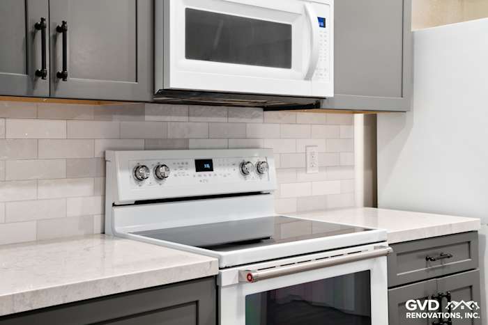 Modern kitchen detail featuring a white stove and microwave, gray cabinets, and subway tile backsplash
