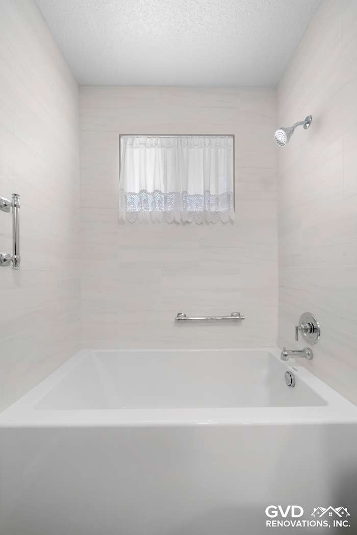 Modern bathtub with tiled walls and a lace curtain, featuring a sleek showerhead in a renovated bathroom