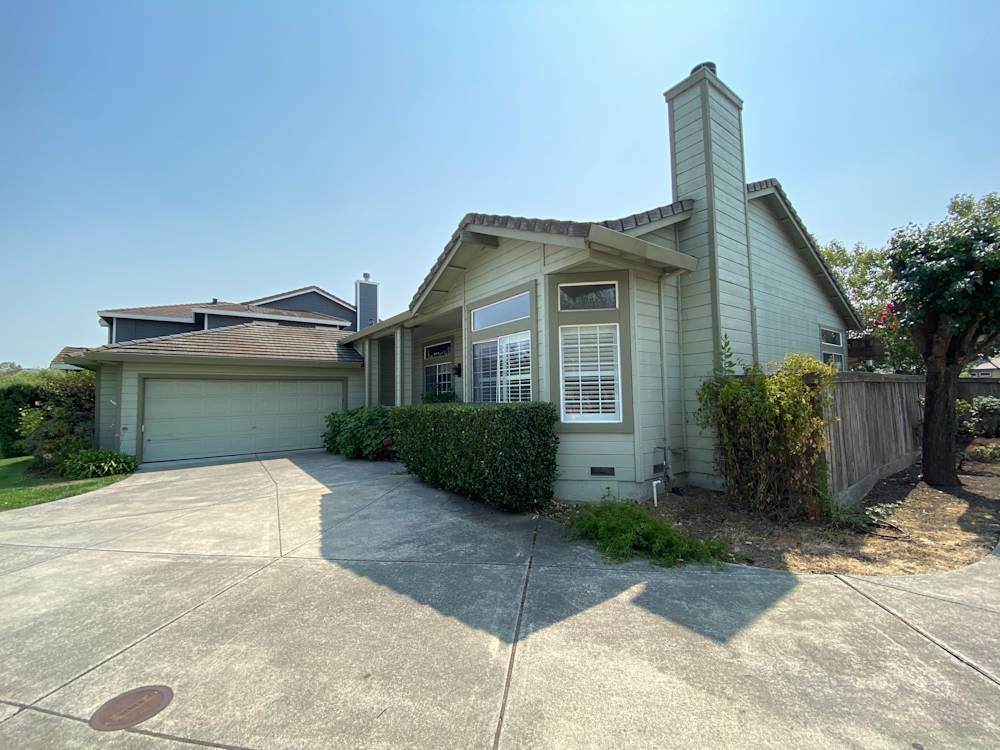 Single-story home with light green siding, concrete driveway, and well-maintained landscaping in Sacramento