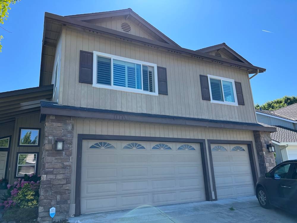 Dated exterior with beige wood siding and light garage doors