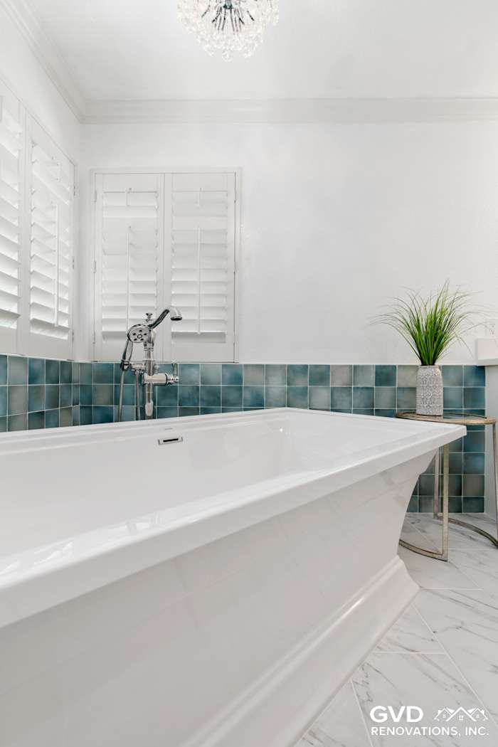 Modern bathroom featuring a freestanding white soaking tub, teal subway tile, and a sleek chandelier