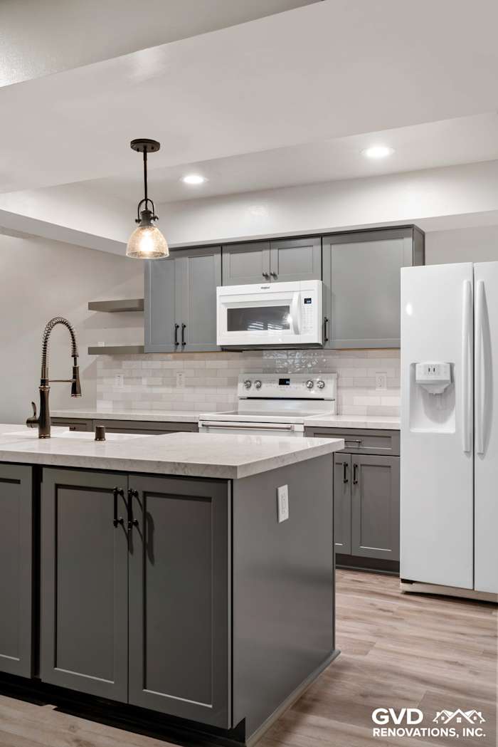 Modern kitchen remodel featuring gray cabinets, quartz countertop, stainless steel appliances, and pendant lighting