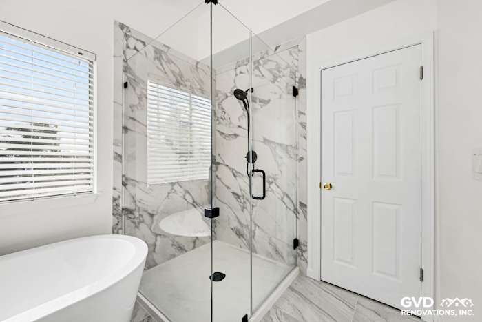 Modern bathroom remodel featuring a glass walk-in shower with marble walls and a freestanding tub in Sacramento
