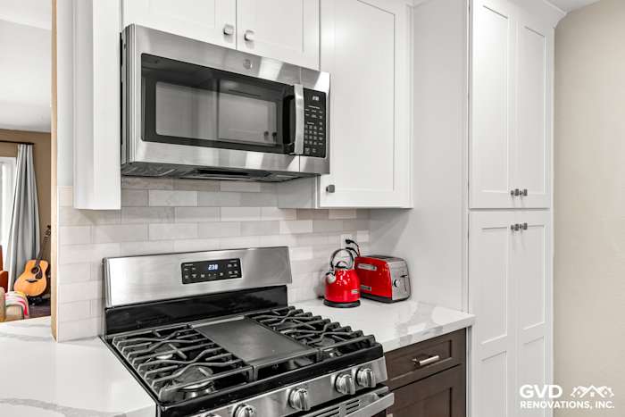 Modern kitchen with stainless steel appliances, white cabinets, and quartz countertop, featuring a sleek microwave and gas