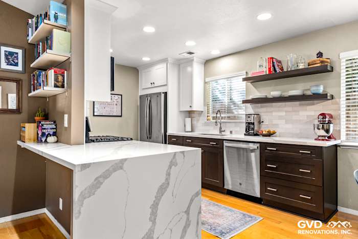 Modern kitchen with a marble island, dark wood cabinetry, stainless steel appliances, and natural light from windows