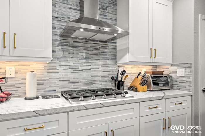 Modern kitchen featuring Cambria custom countertops, white cabinetry, gray glass backsplash, and stainless steel appliances
