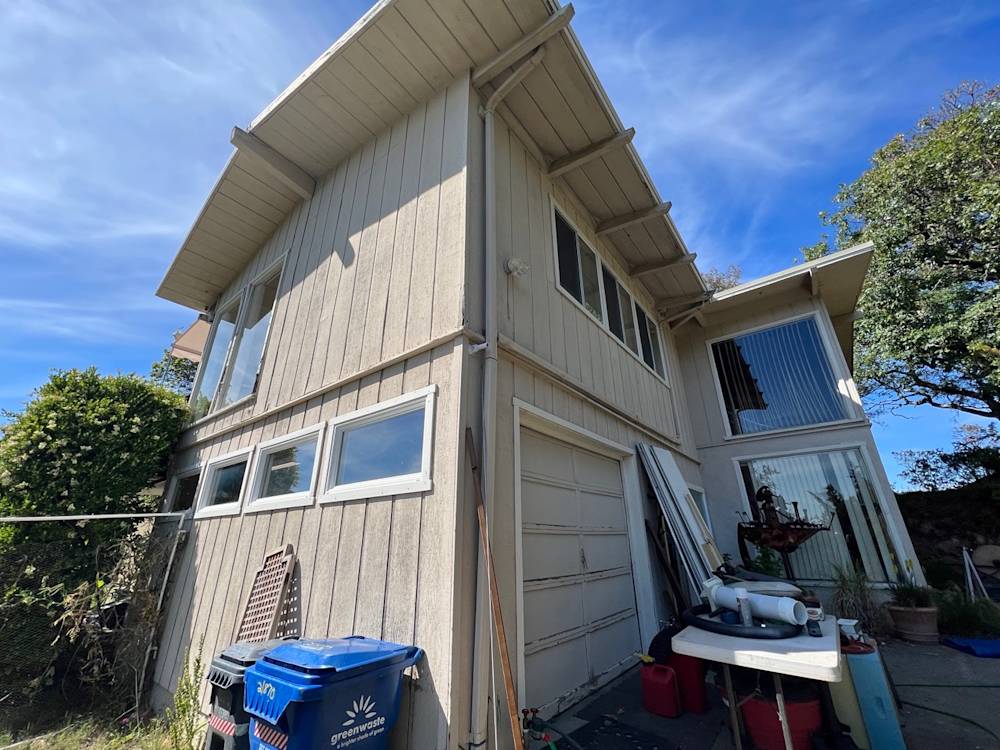 Side view of a two-story home in Sacramento with a gray exterior and cluttered yard features