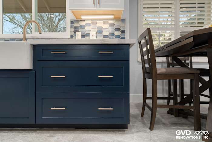 Navy blue kitchen island with white farmhouse sink, gray tile flooring, and modern light fixtures