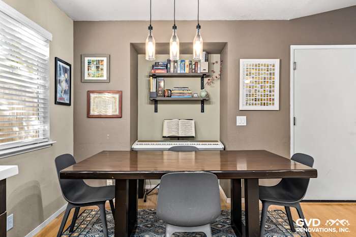 Modern dining area with wooden table, black chairs, decorative shelving, and pendant lights