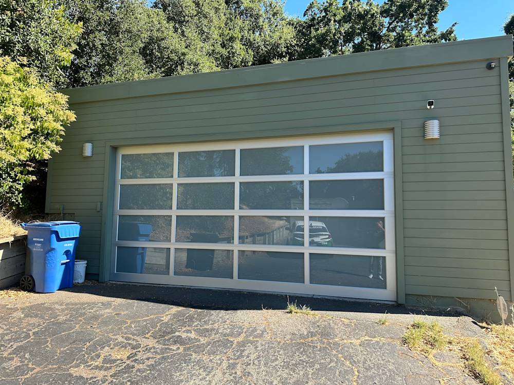 Modern garage with large glass doors and green siding in Sacramento, surrounded by lush trees