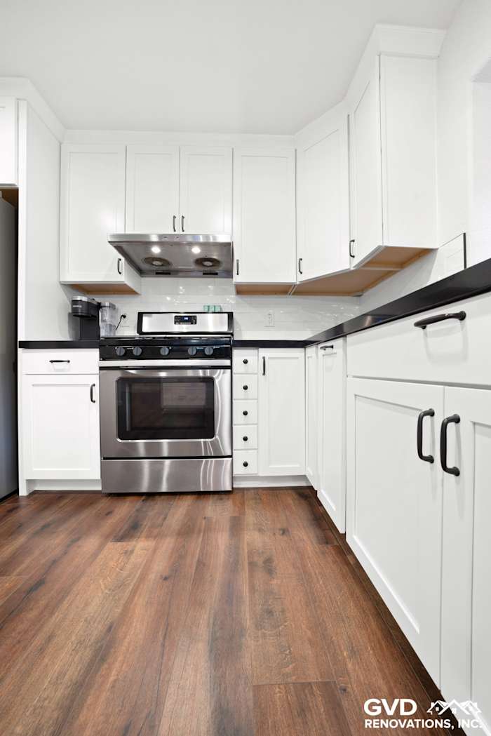 White shaker cabinets with stainless steel appliances, black countertops, and wood flooring in remodeled kitchen